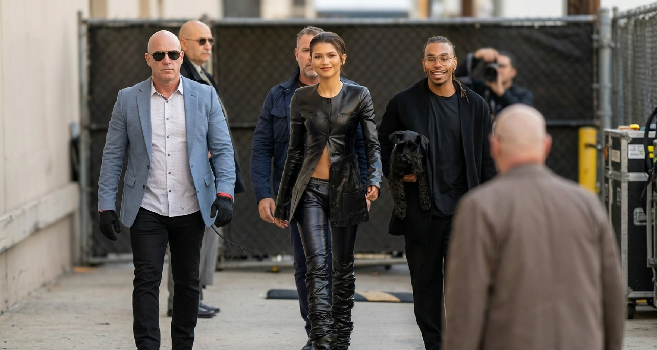 Zendaya wearing The Attico SS24 black leather collarless longline jacket with asymmetrical button closure, slim-fit silhouette, and V-shaped flare.