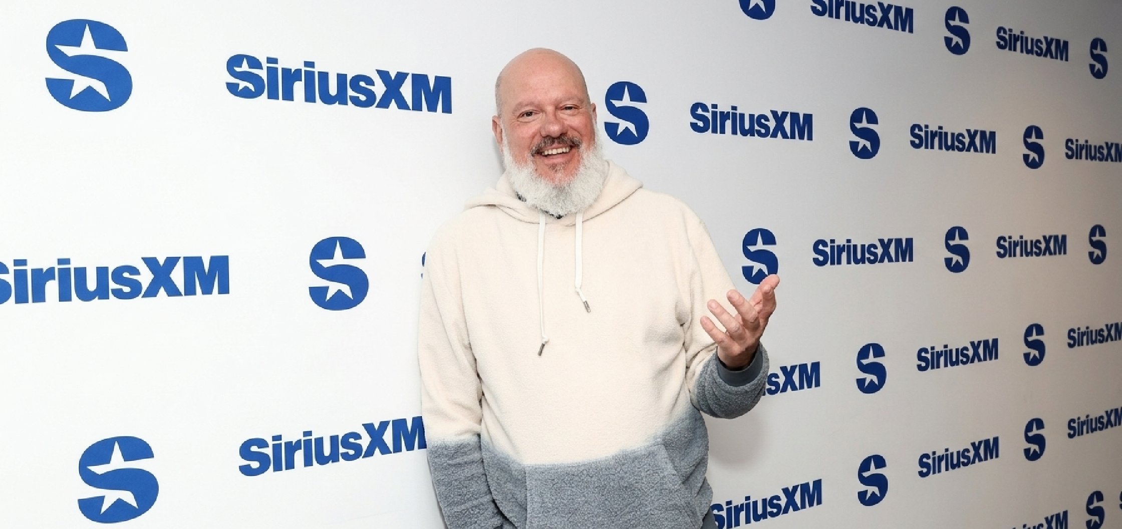 David Cross wearing SiriusXM Studios 2026 cream-to-grey dip-dye pullover hoodie with sherpa fleece texture and relaxed fit in New York studio setting