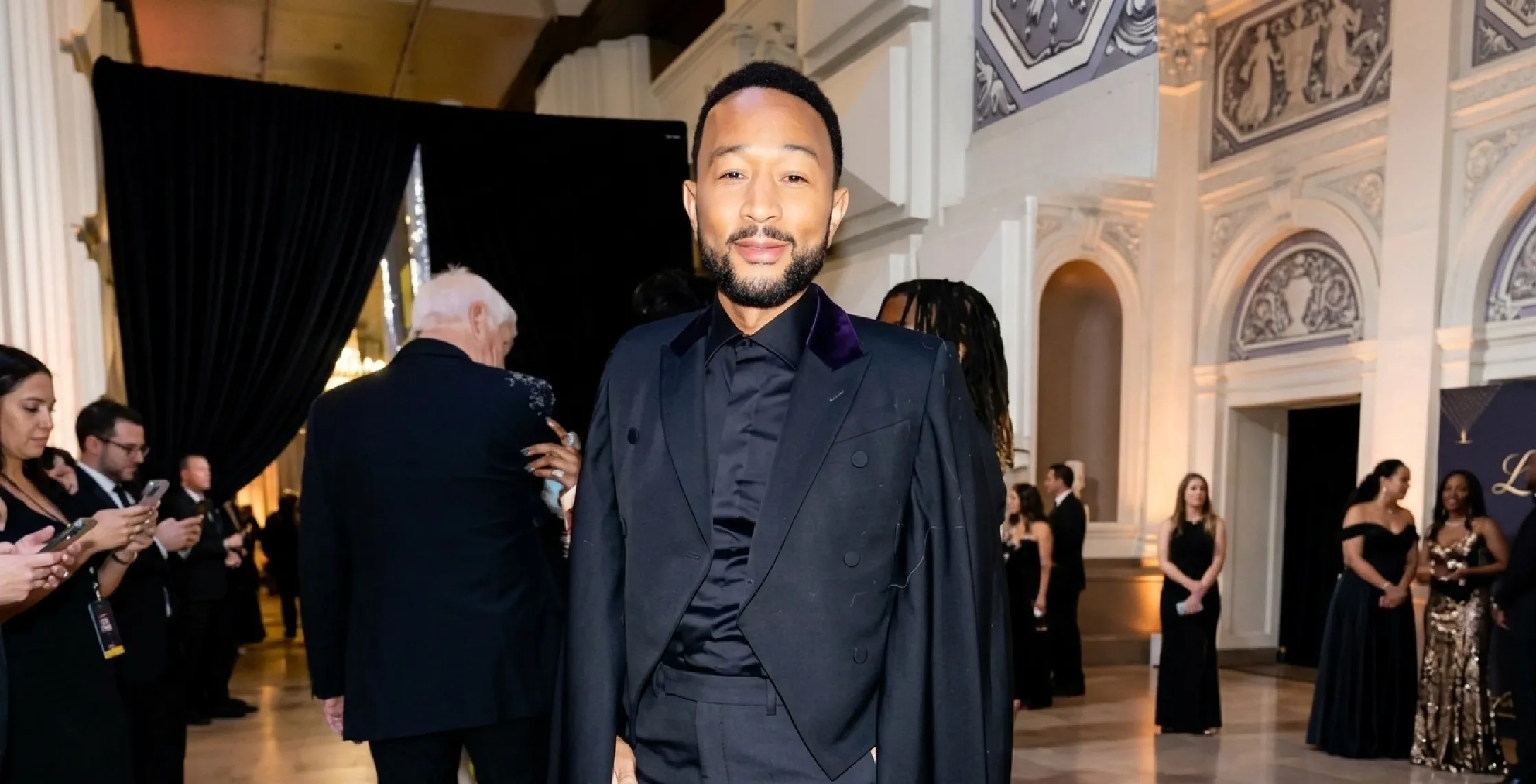 John Legend wearing a black cropped double-breasted blazer with purple velvet peak lapels and cape-style sleeves at Cats The Jellicle Ball event