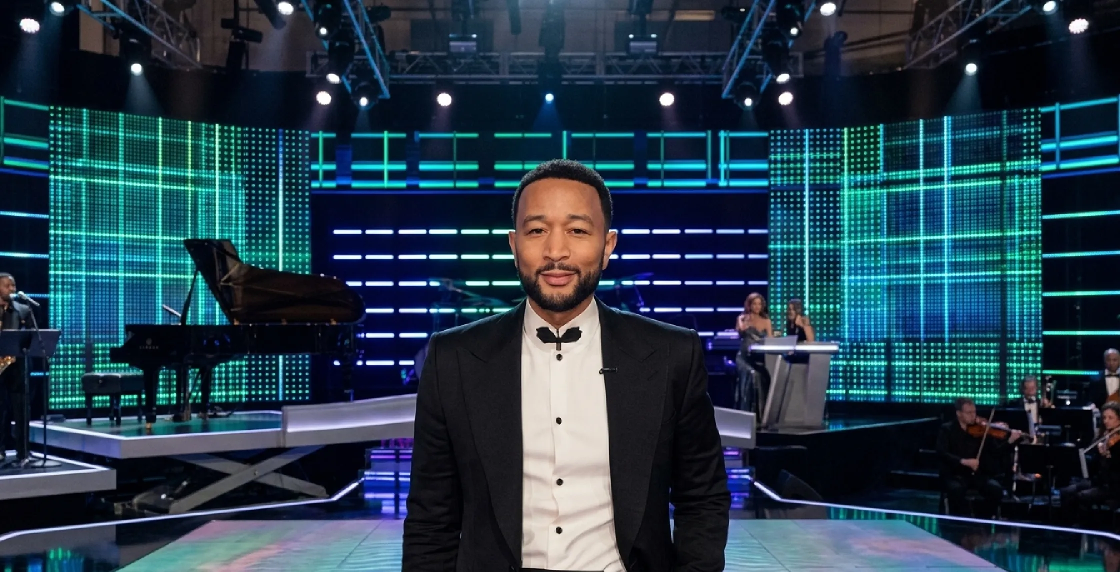 John Legend wearing a black cropped double-breasted blazer with purple velvet peak lapels and cape-style sleeves at Cats The Jellicle Ball event