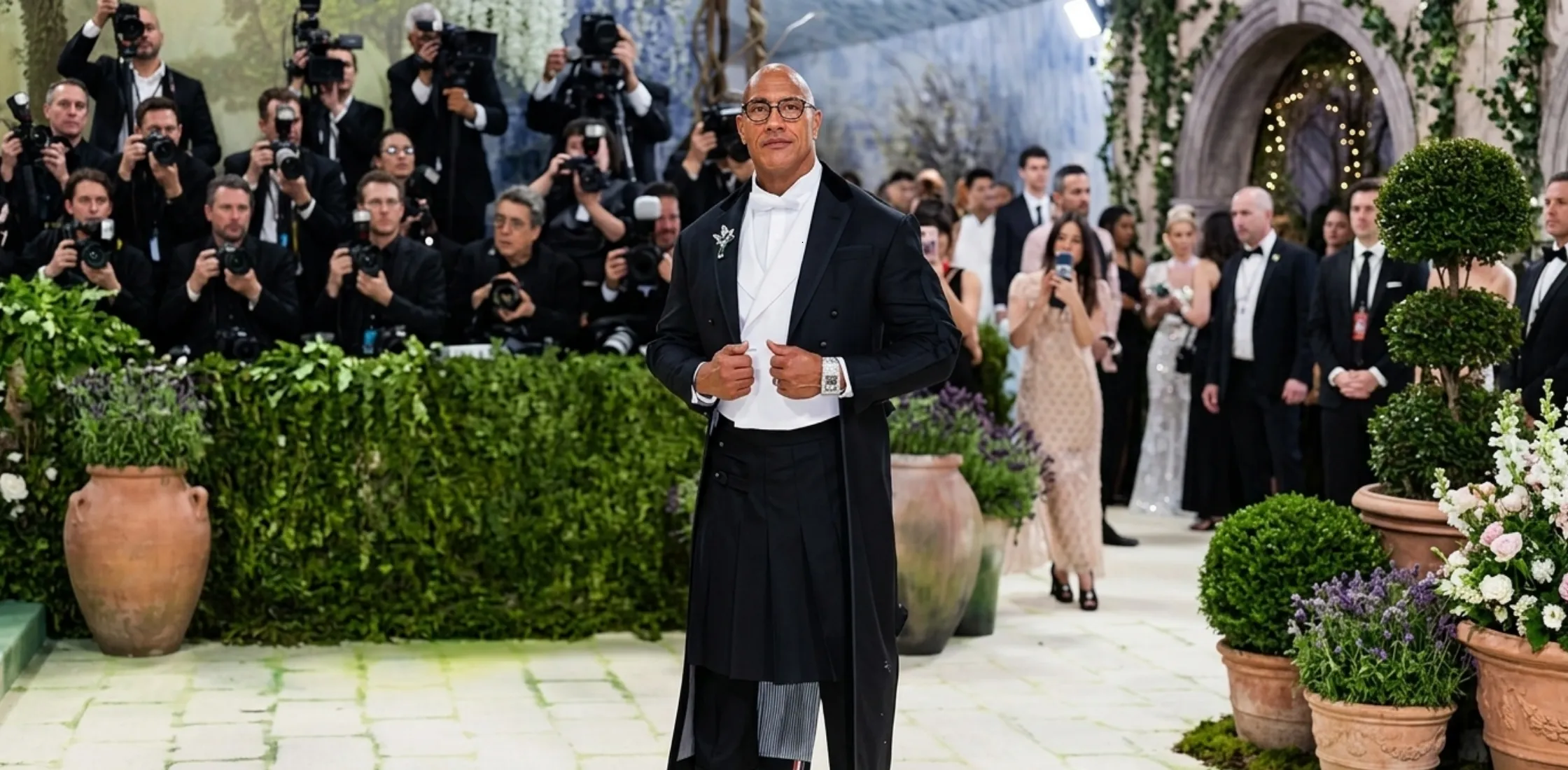 Dwayne Johnson wearing the 2026 Met Gala black velvet frock coat with pleated skirt overlay, white waistcoat, and formal red-carpet accessories