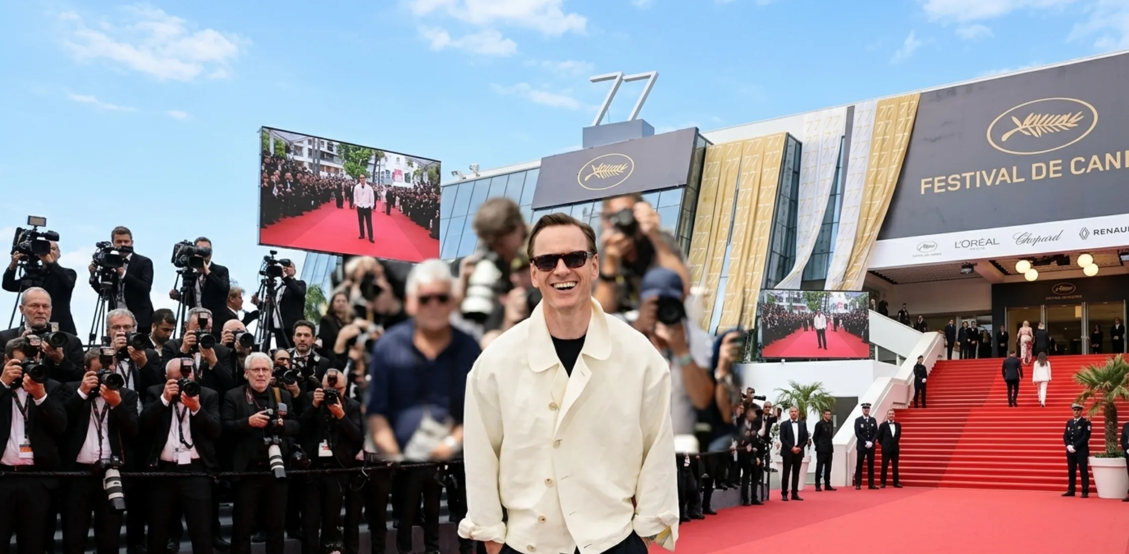 Michael Fassbender wearing a cream asymmetrical blouson jacket at the 79th Cannes Film Festival, styled with navy trousers and a black T-shirt, showcasing Riviera-inspired menswear elegance.