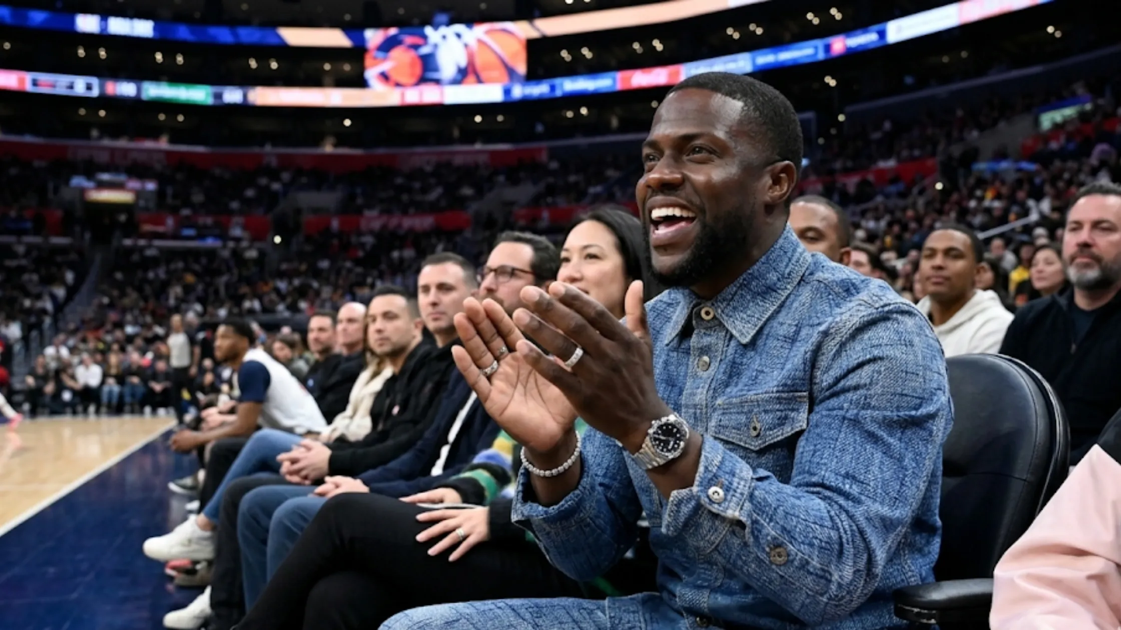 Kevin Hart sitting courtside at a Los Angeles Lakers game wearing an indigo grid-check windowpane denim jacket.
