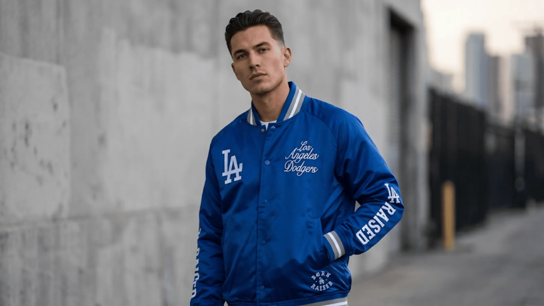A vibrant electric blue Born x Raised LA Dodgers post-season satin bomber jacket featuring intricate white typography branding on the front, back, and sleeves with classic striped ribbed trim.