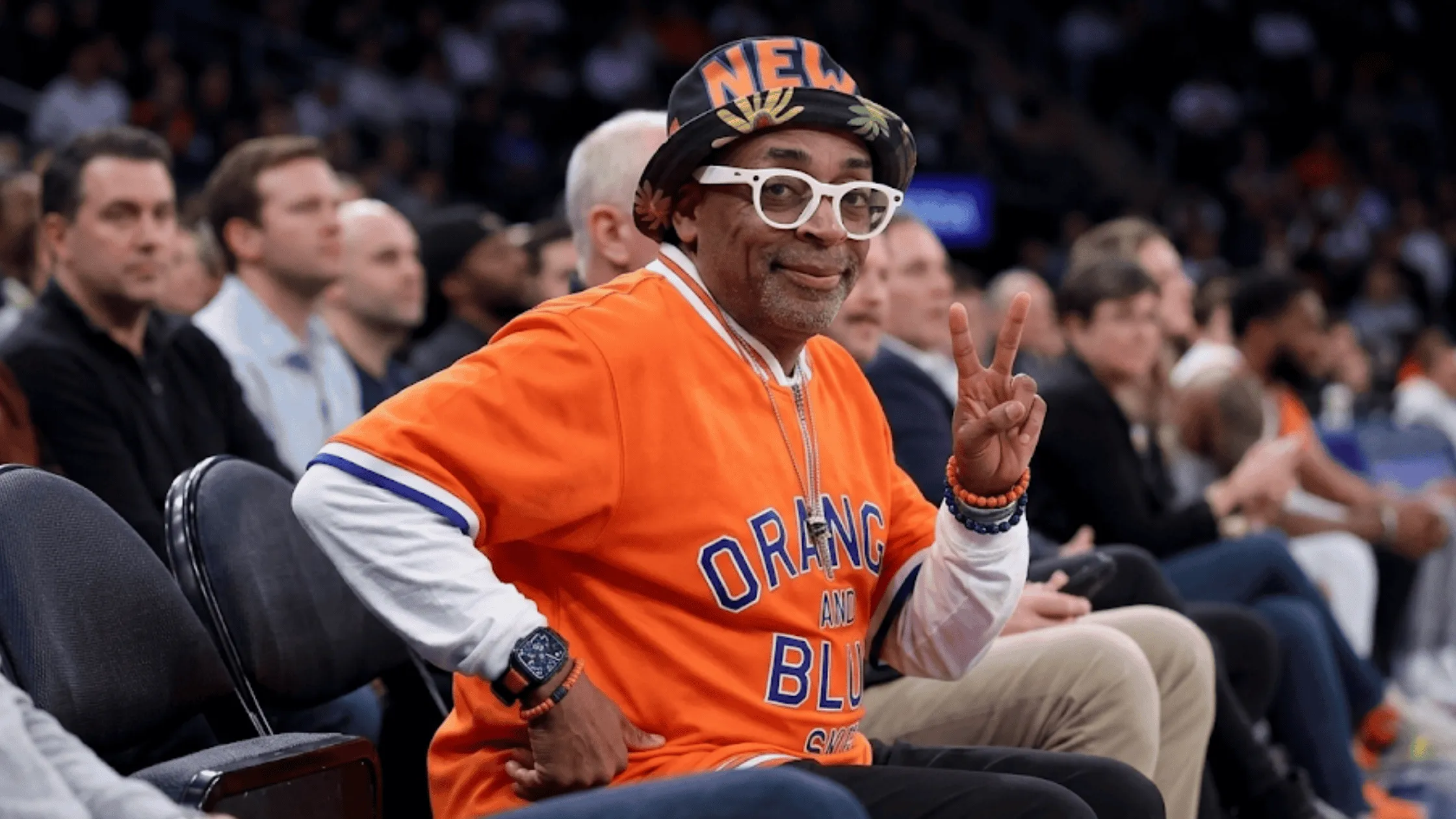 Spike Lee wearing the New York Knicks vs Atlanta Hawks Orange and Blue Skies quarter-zip short sleeve pullover shirt courtside.
