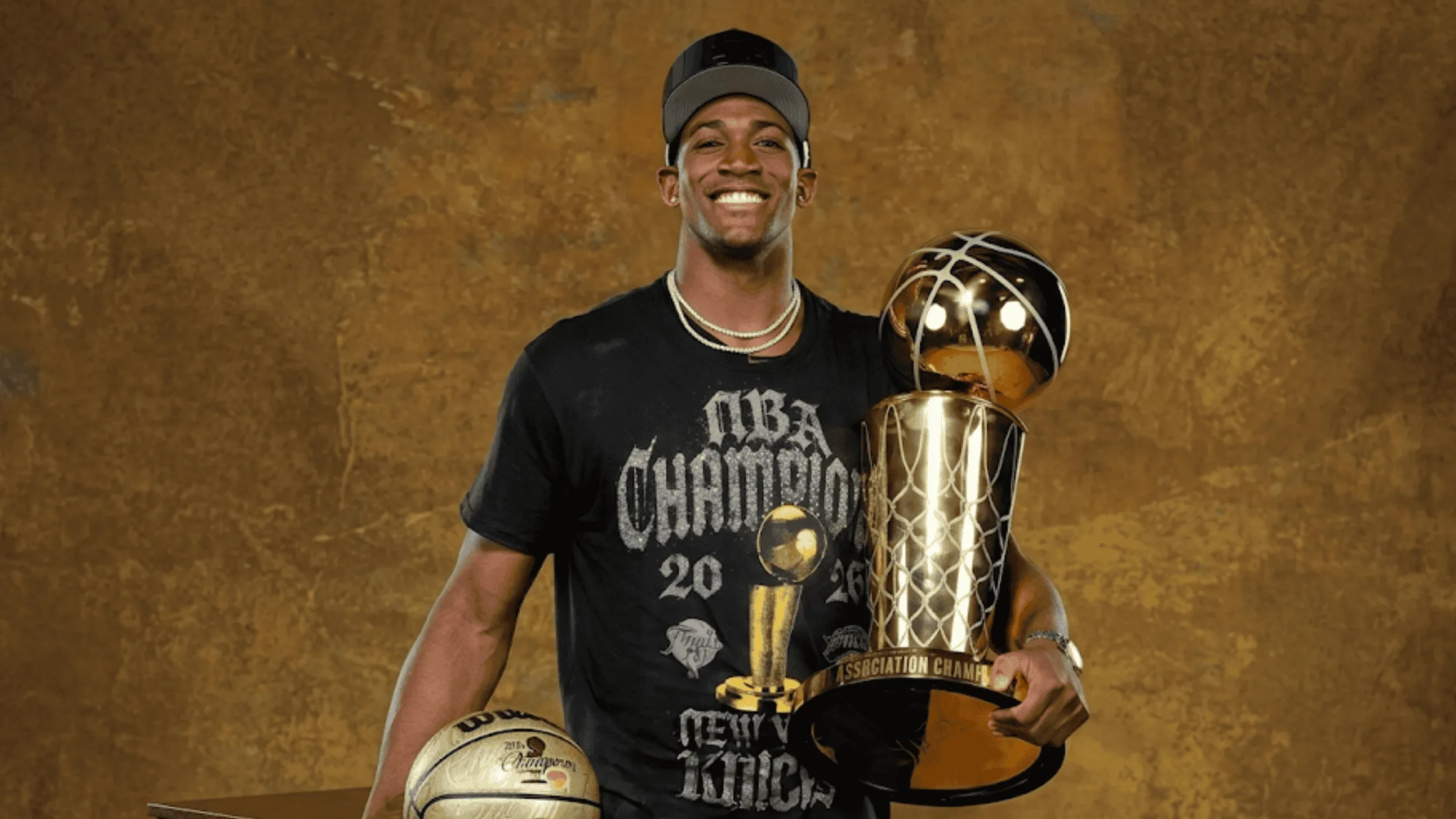 Trey Jemison wearing the New York Knicks 2026 NBA Champions black crewneck t-shirt featuring a metallic gold Larry O'Brien trophy graphic and gothic script.
