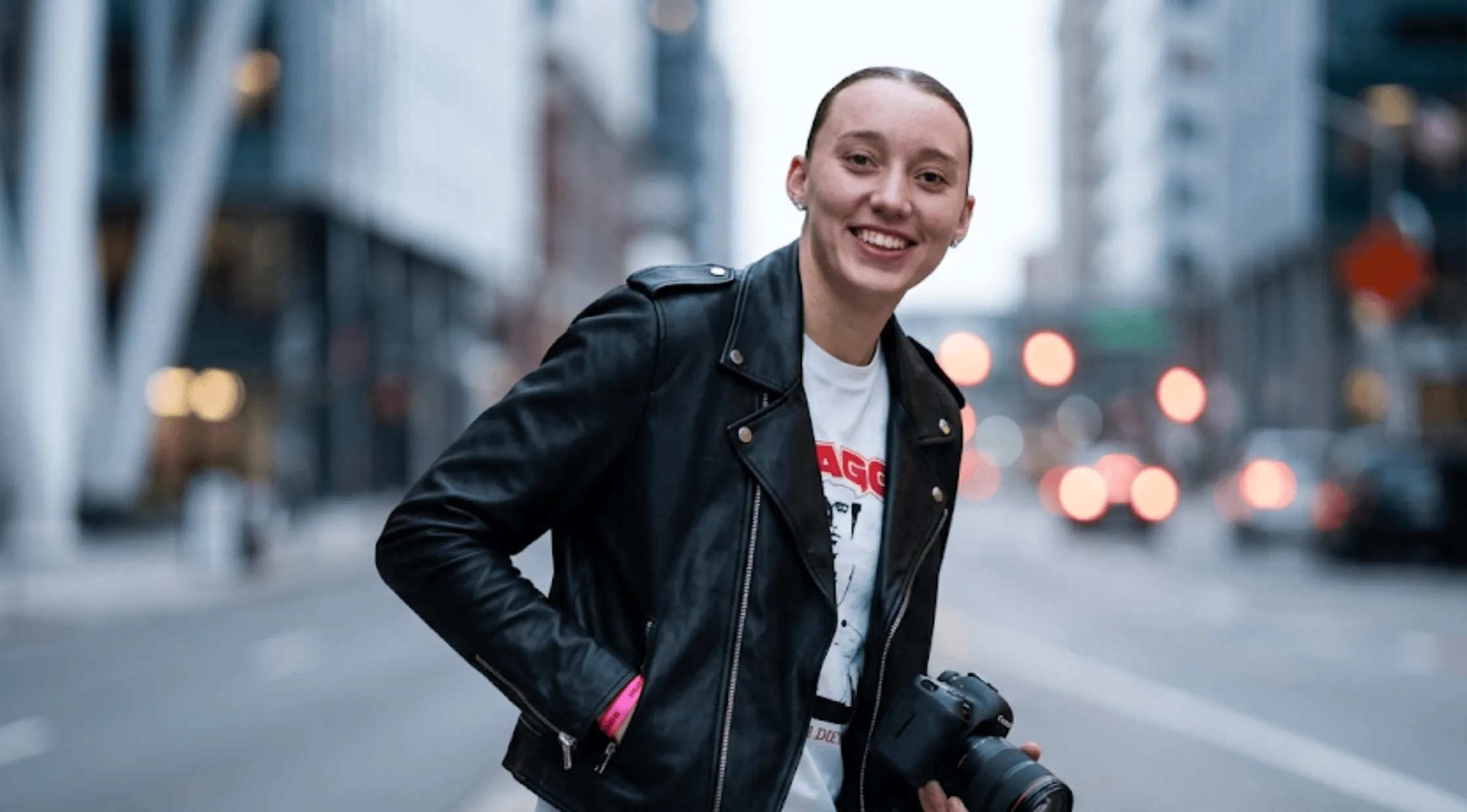 Paige Bueckers wearing a black asymmetrical leather biker jacket with silver hardware, wide notch lapels, and shoulder epaulets over a white graphic tee.