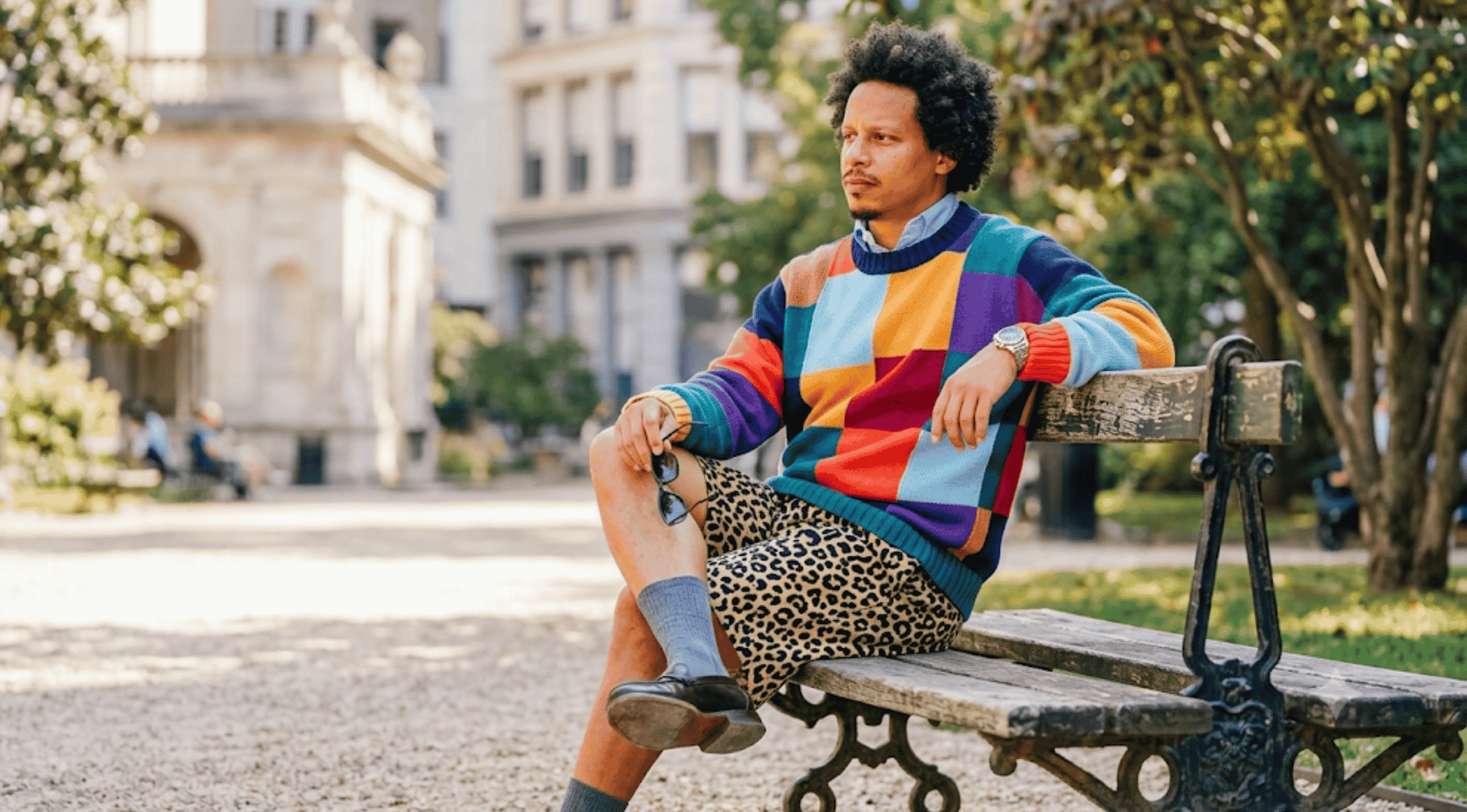 Eric André wearing the multicolored patchwork geometric colorblock crewneck pullover sweater featuring navy, sky blue, purple, green, orange, and yellow knit panels.