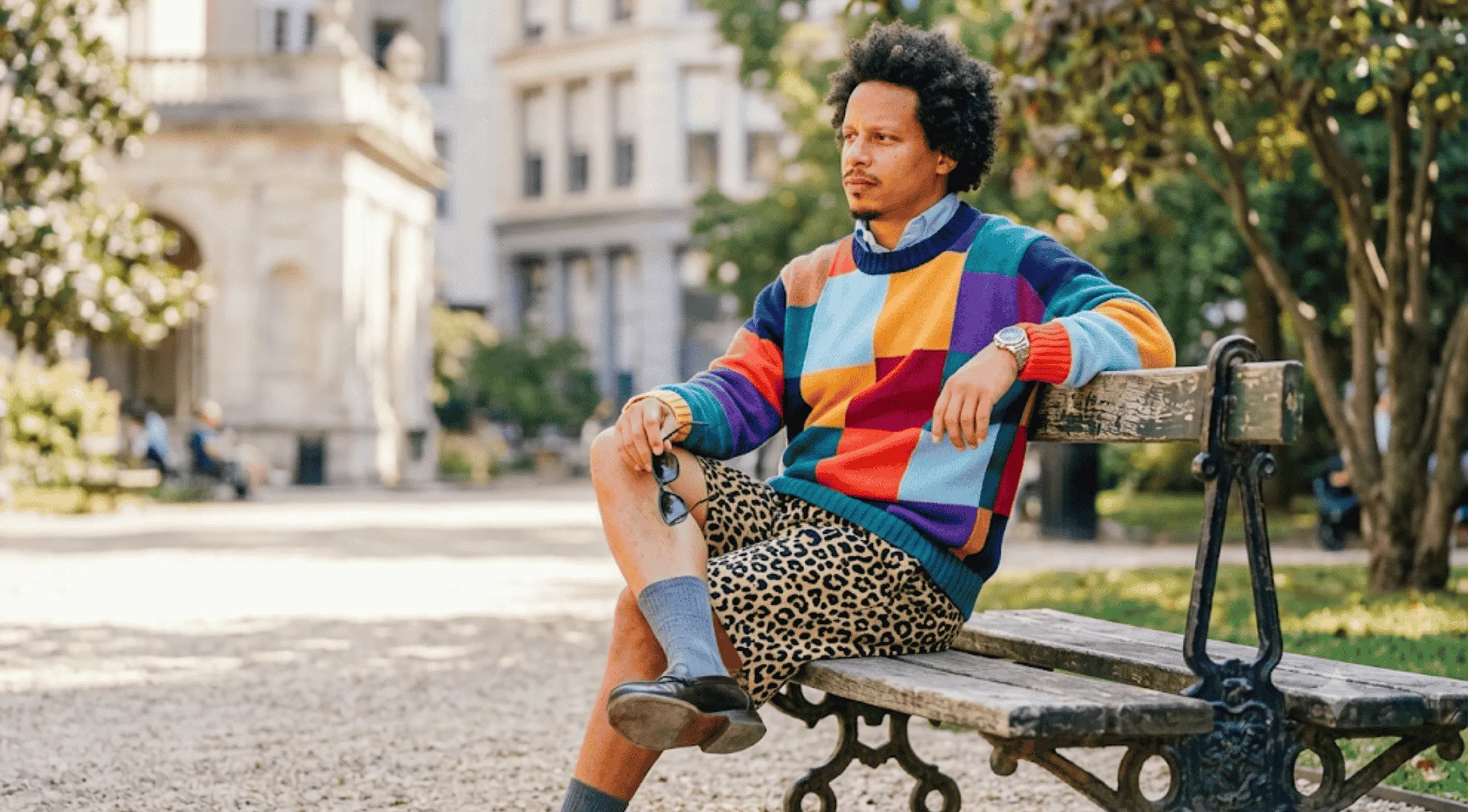 Eric André wearing the multicolored patchwork geometric colorblock crewneck pullover sweater featuring navy, sky blue, purple, green, orange, and yellow knit panels.