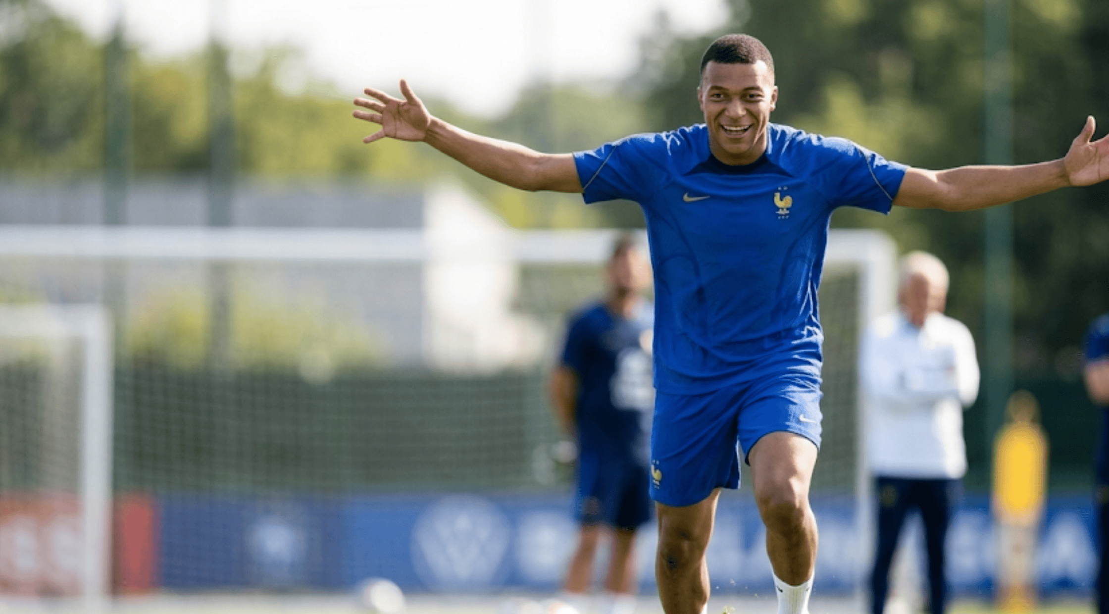 A person wearing the royal blue Kylian Mbappé France FIFA World Cup 2026 performance T-shirt with the FFF golden rooster crest and a navy blue shoulder panel.
