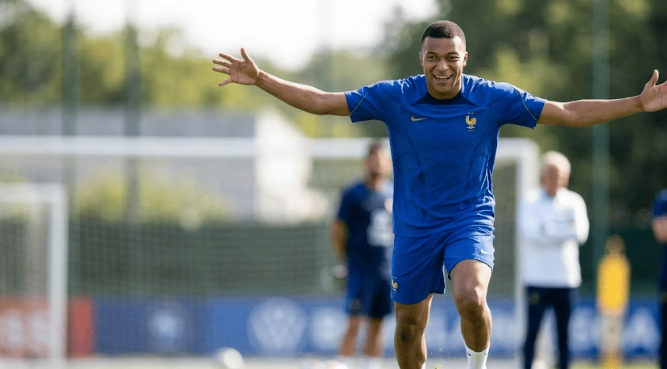 A person wearing the royal blue Kylian Mbappé France FIFA World Cup 2026 athletic T-shirt featuring the golden-brown FFF rooster crest and a deep navy shoulder panel.
