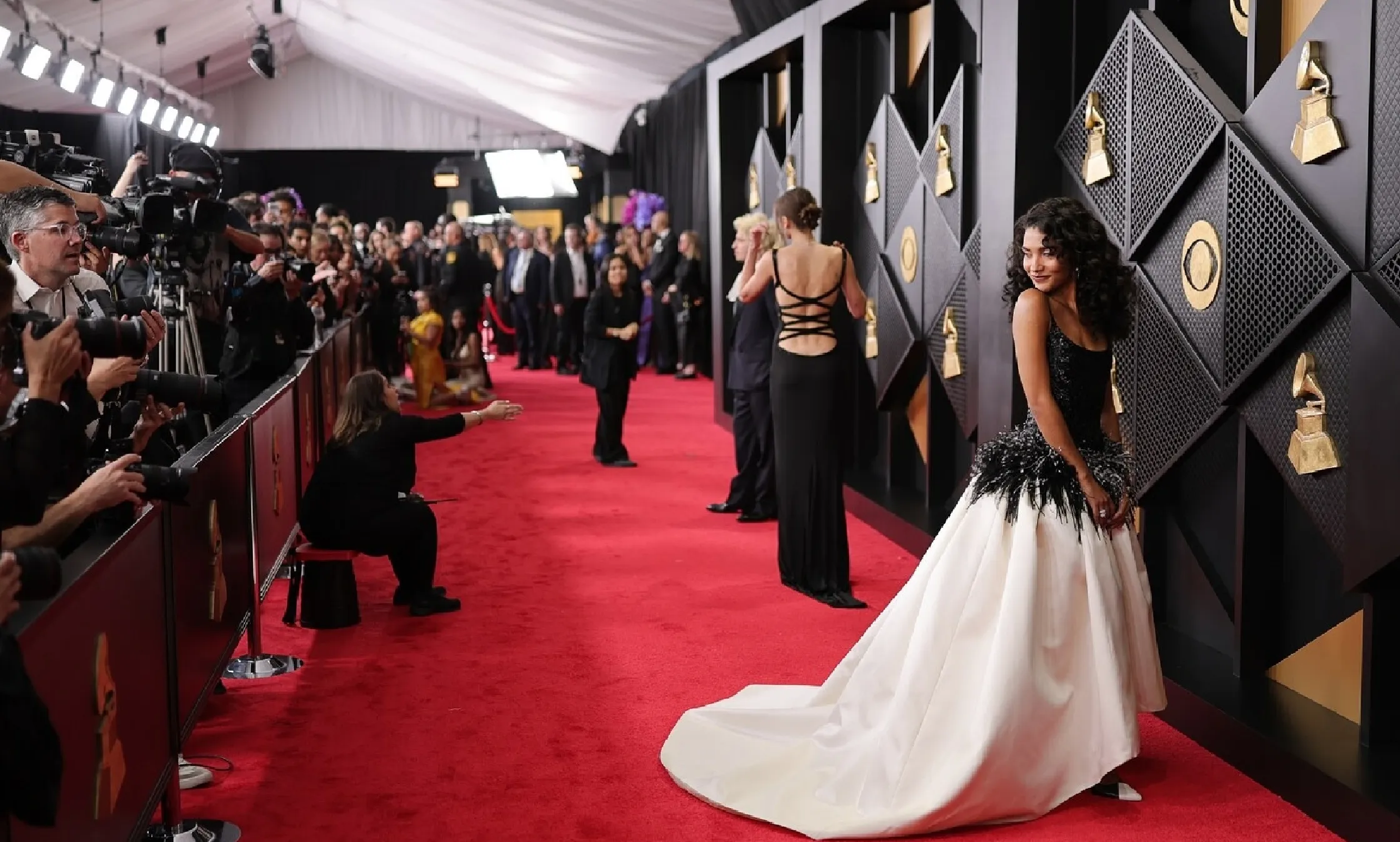 Celebrity posing on the red carpet at the 68th GRAMMY Awards 2026 in a black and white gown with feather detailing, surrounded by photographers and media