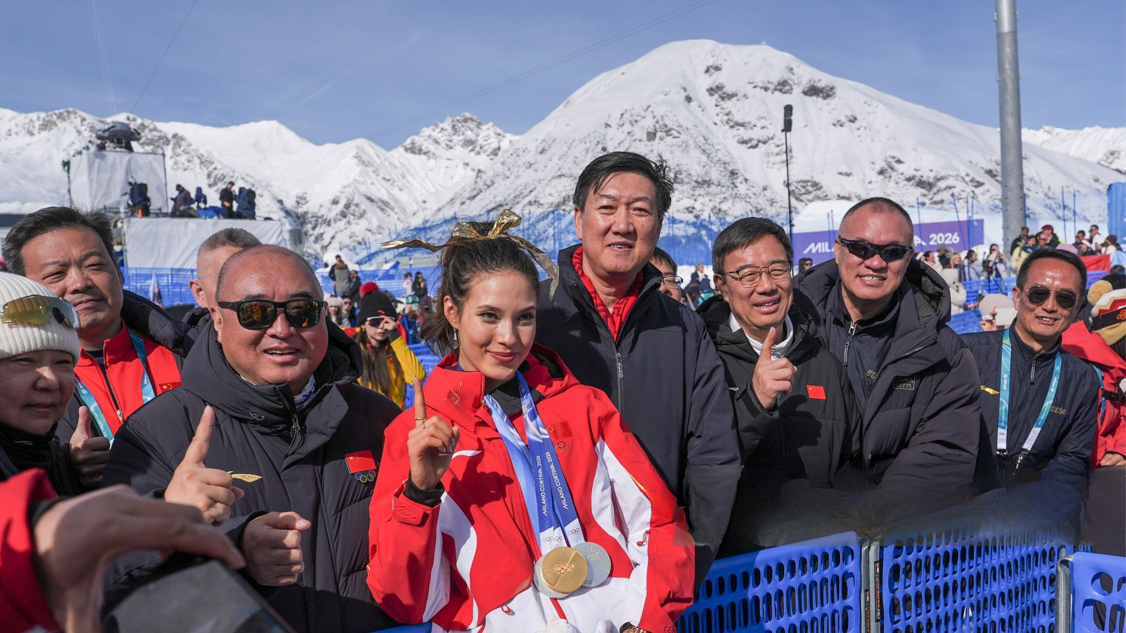 Ailing Eileen Gu wearing cherry red and white Winter Olympics 2026 freestyle skiing jacket with gold accents