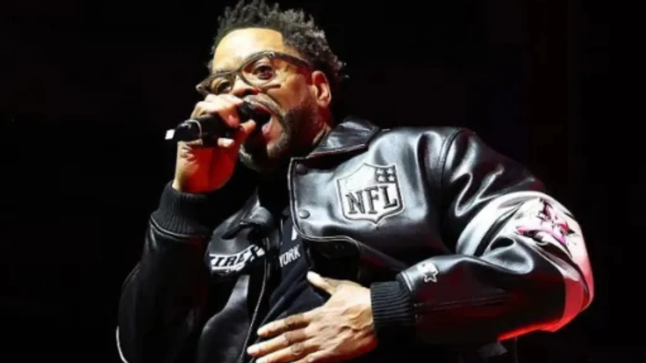 Method Man performs on stage wearing a black leather varsity jacket with NFL and Avirex logos, reflecting stage lights.