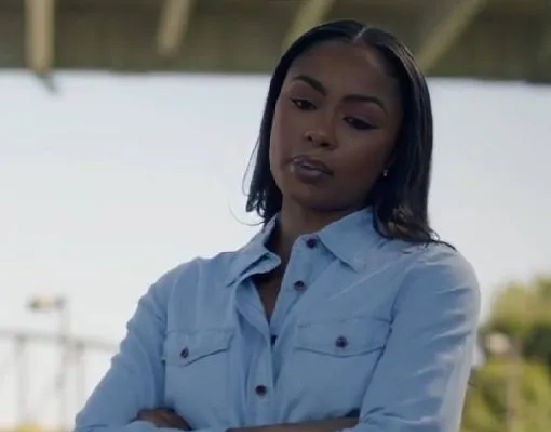 Brittany wearing a light blue button-up shirt with tied hem and high-waisted jeans in Checkmate (2025)