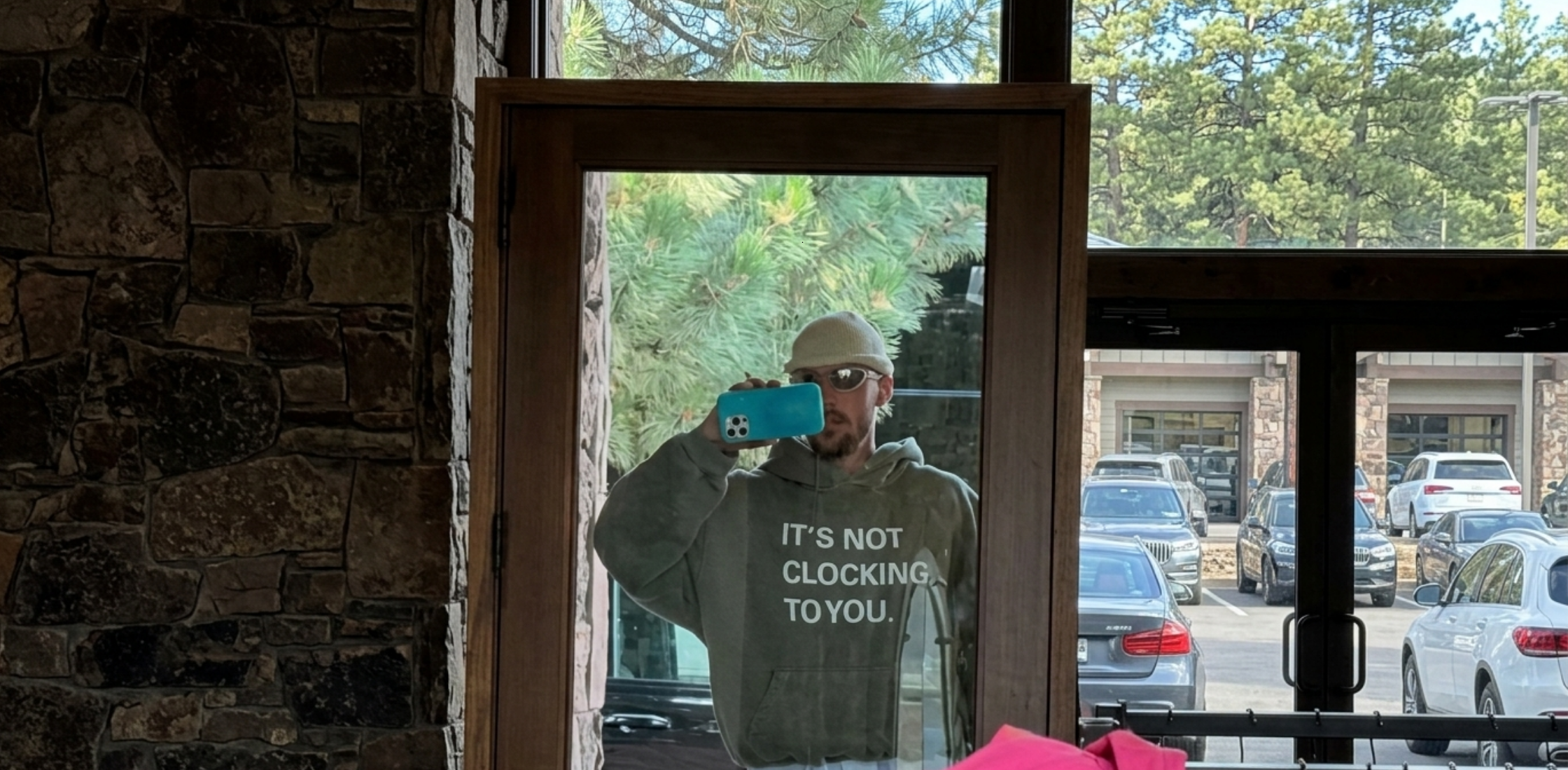 It’s Not Clocking To You olive green hoodie with bold white text graphic front design, oversized streetwear fit, minimal modern pop culture inspired sweatshirt with kangaroo pocket and hood.