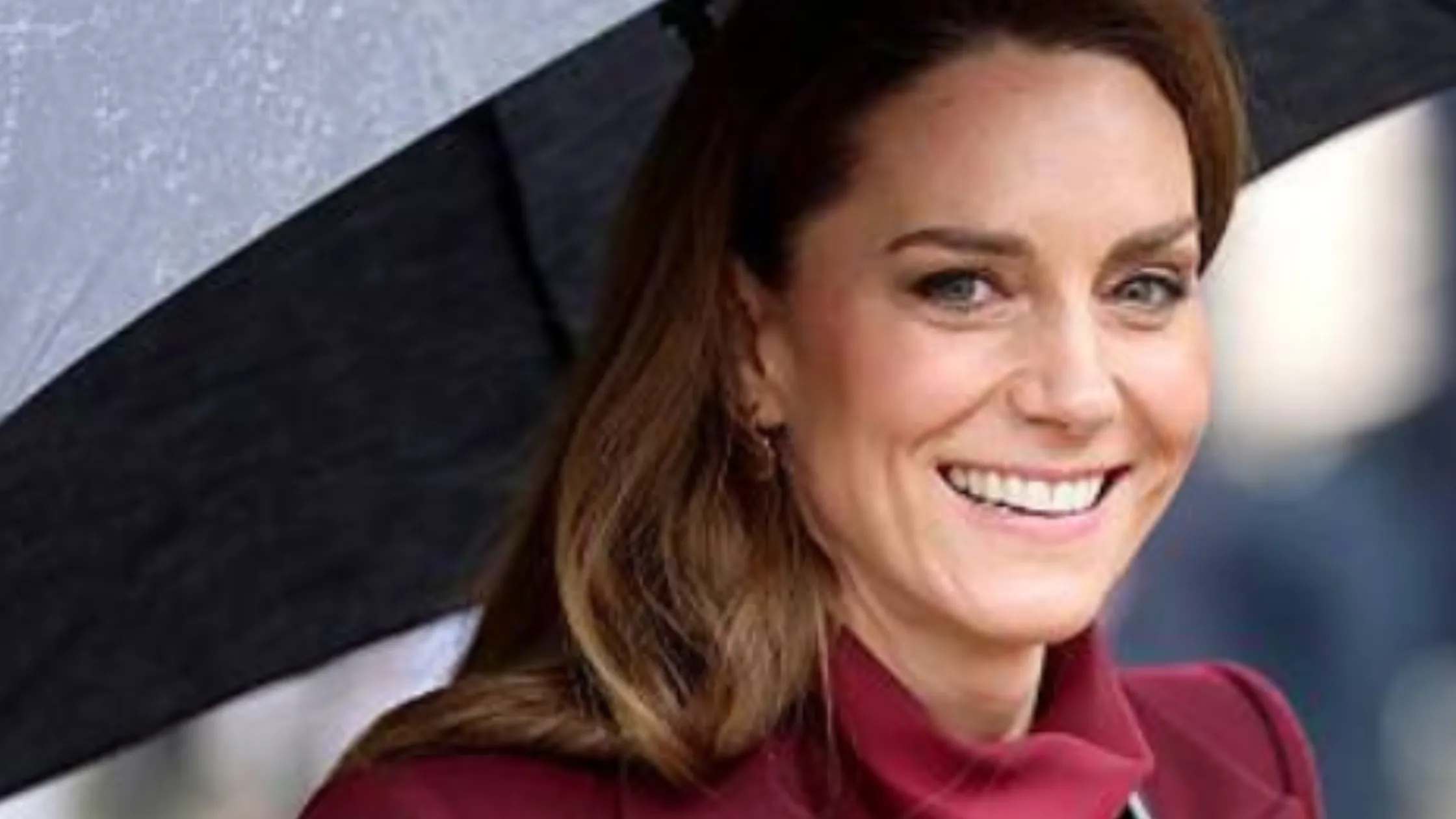 Wales visit star Catherine, Princess of Wales wears a stylish burgundy maxi coat, adding a pop of color to the rainy day.