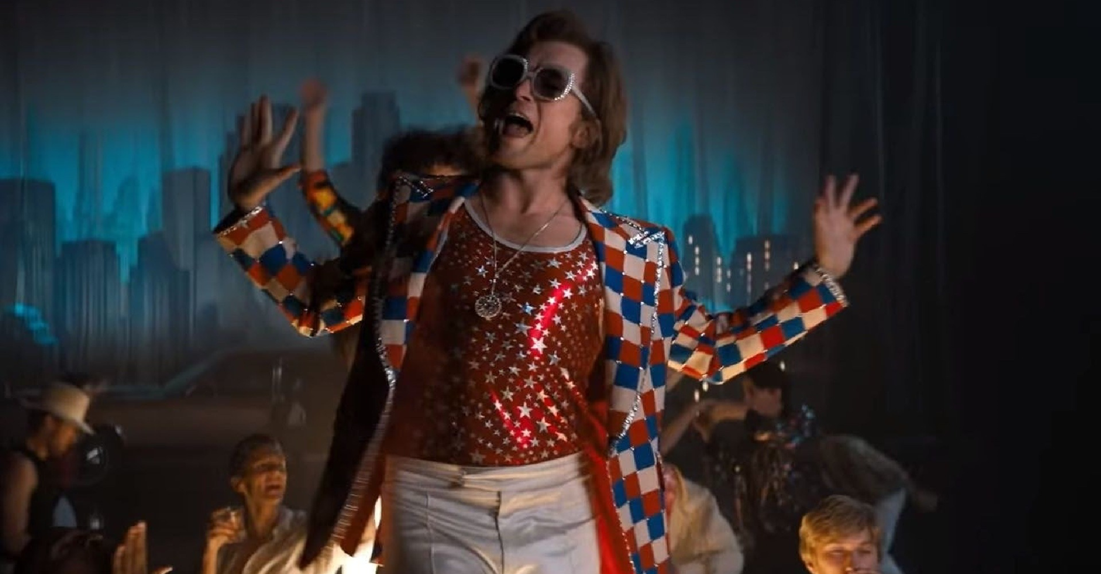 Unisex Rocketman Elton John red, blue, and white checked blazer with silver stud embellishments, wide notched lapels, and padded shoulders, styled with a white top and dark trousers.