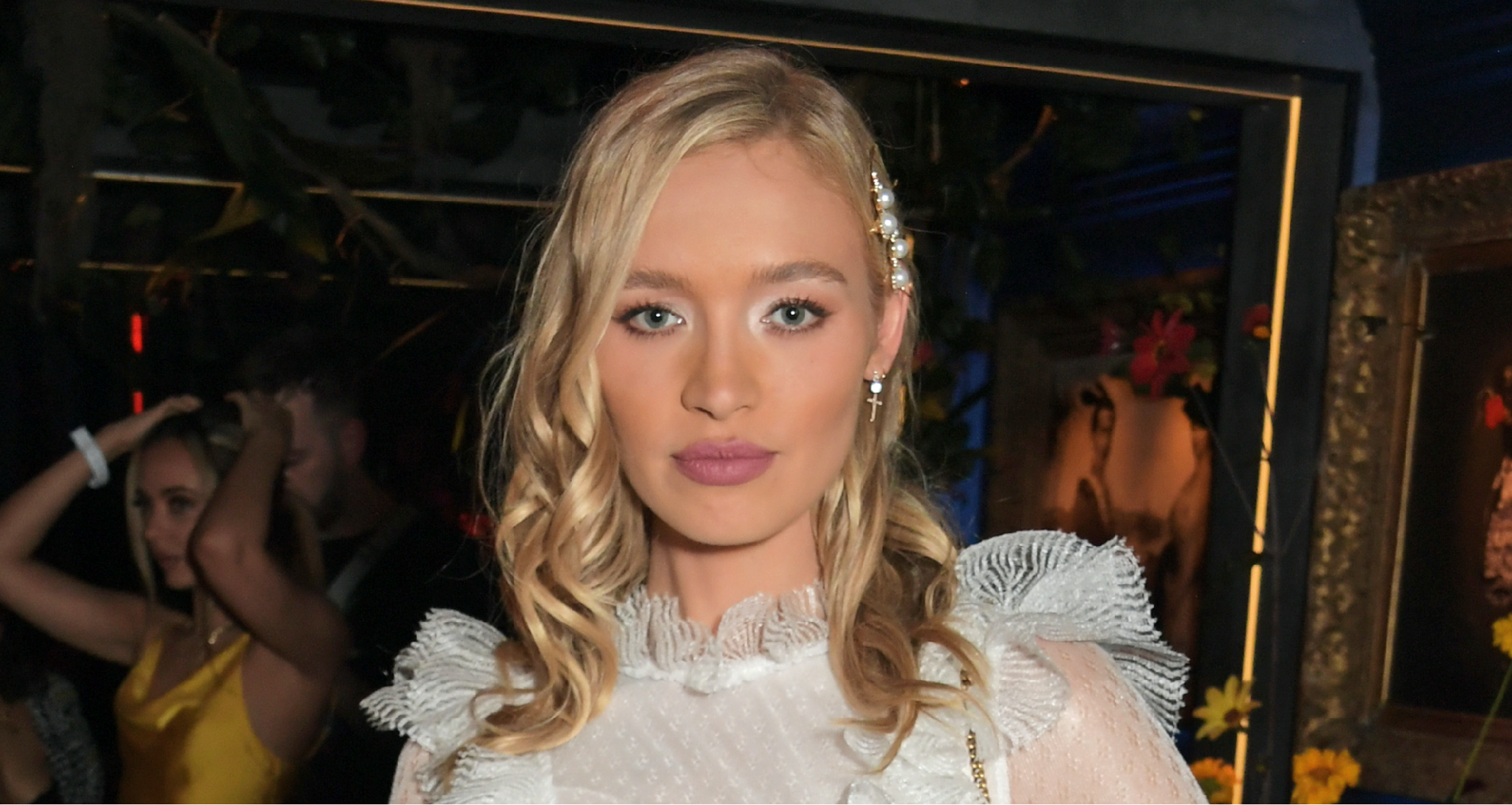 Roxy Horner wearing a taupe structured blazer with deep brown satin lapels over a white ruffled blouse, paired with black fitted trousers, styled with loose blonde waves and minimal evening makeup while arriving for a birthday night out in London.