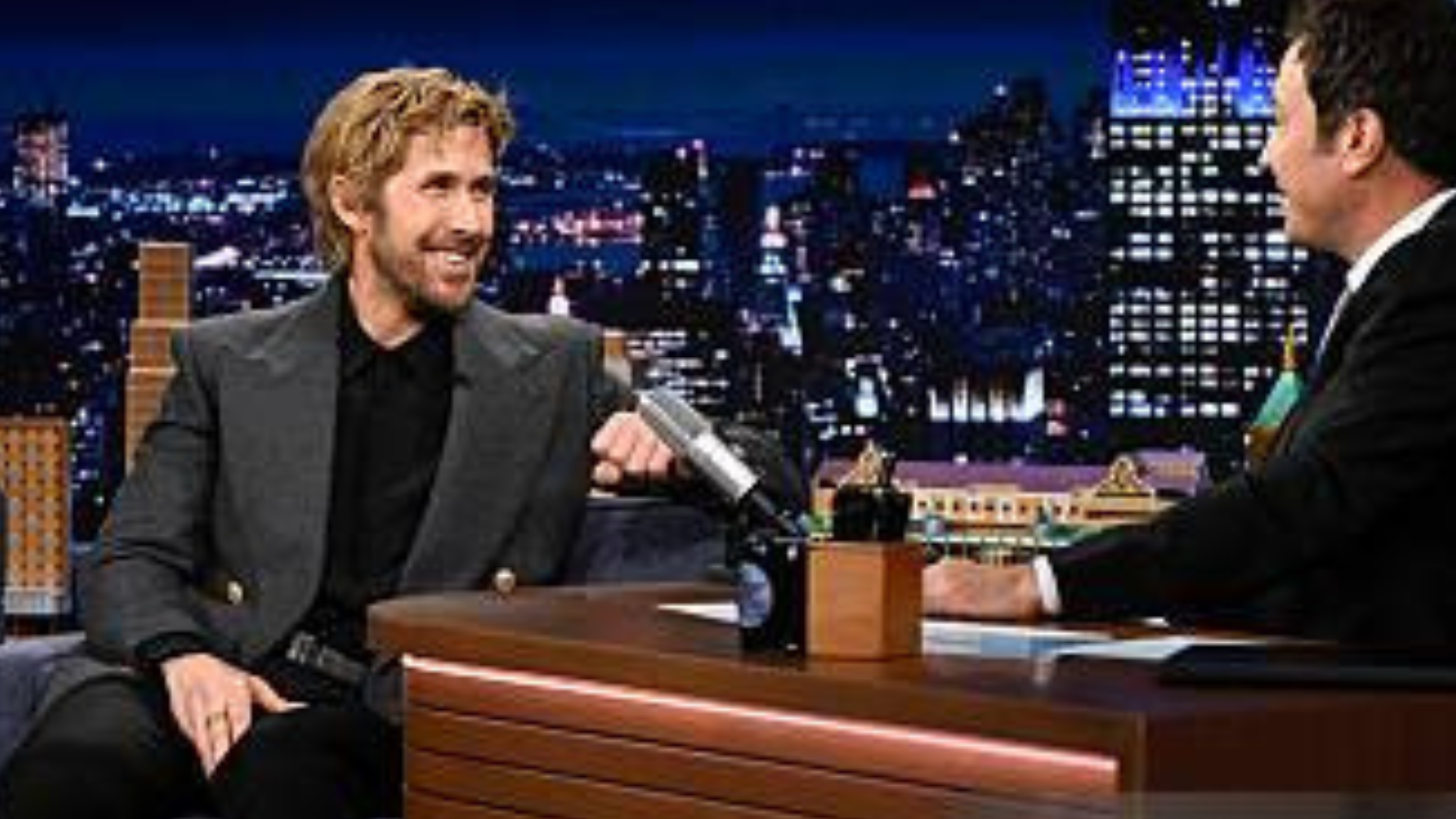 Ryan Gosling wearing a charcoal grey double-breasted blazer with gold buttons during his appearance on The Tonight Show Starring Jimmy Fallon Season 13.