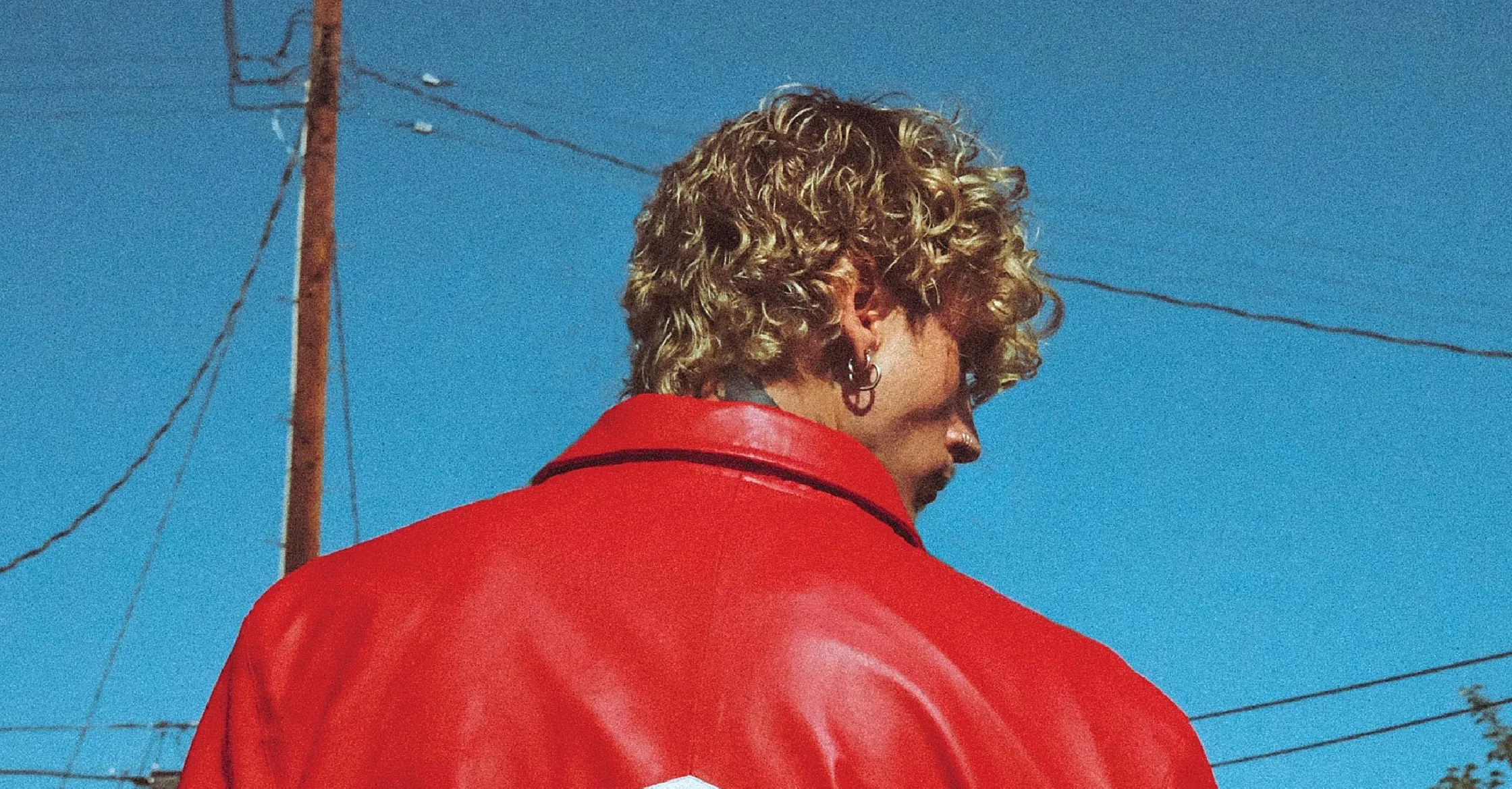 Machine Gun Kelly wearing The Tonight Show MGK Lost Americana Red &amp; White Leather Bomber Jacket featuring bold red and white color blocking, “Lost Americana” black lettering, silver snap buttons, and an Americana sleeve patch