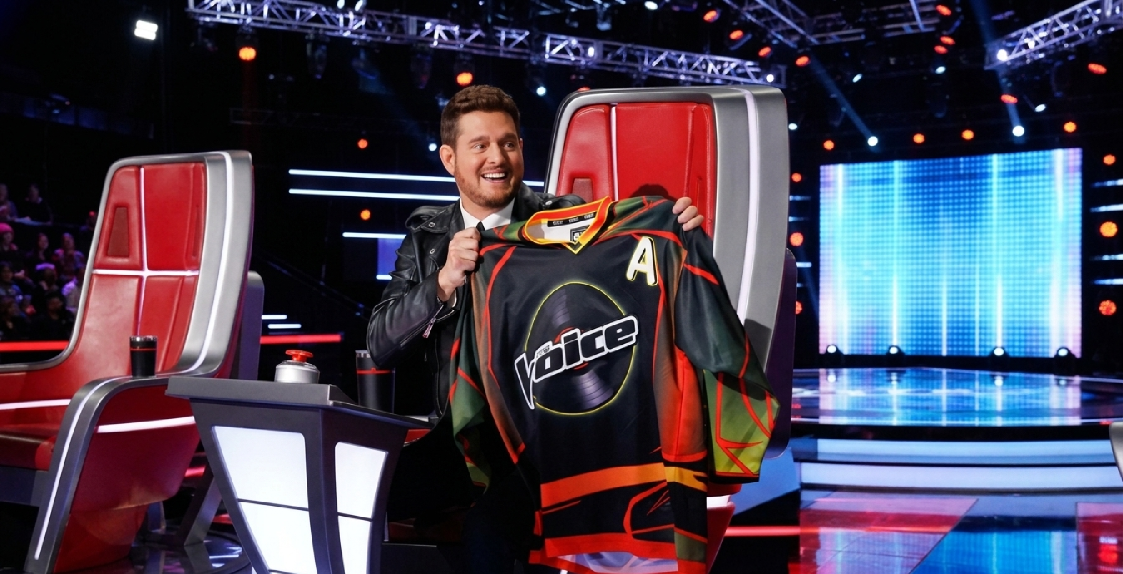 The Voice 2024 Team BublÃ© jersey featuring black base design with vinyl record logo, red yellow green gradient sleeves, and oversized hockey-style fit